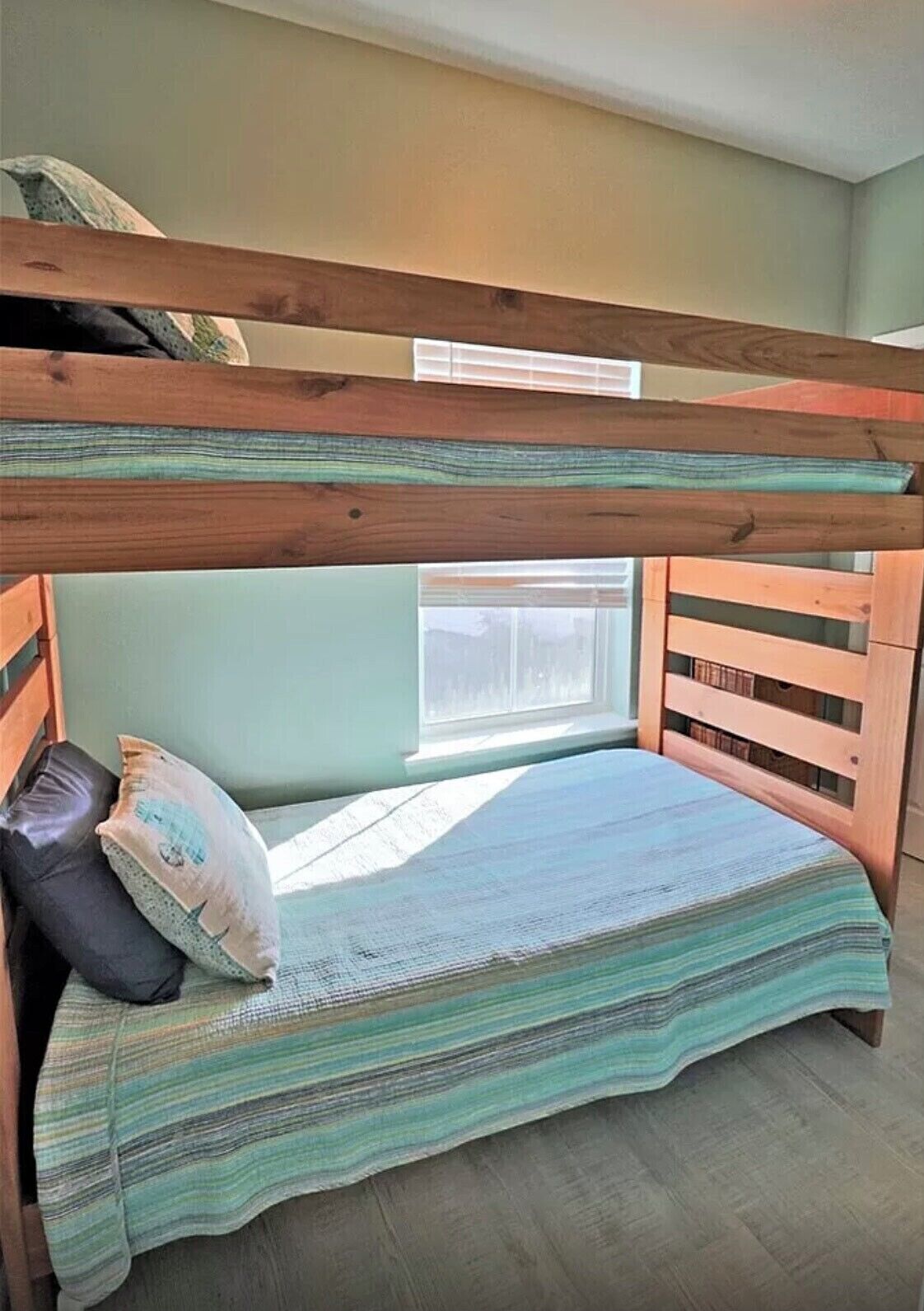 A bunk bed with a striped blanket, pillows, and a window with blinds.