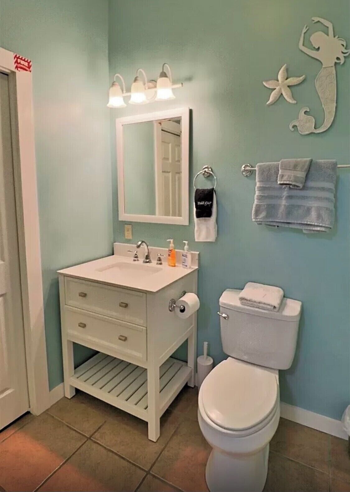 A bathroom with a white vanity, a toilet, and a wall-mounted sink with overhead lighting.