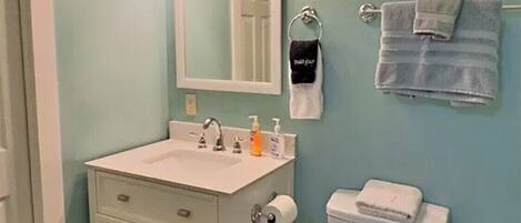 A bathroom with a white vanity, a toilet, and a wall-mounted sink with overhead lighting.