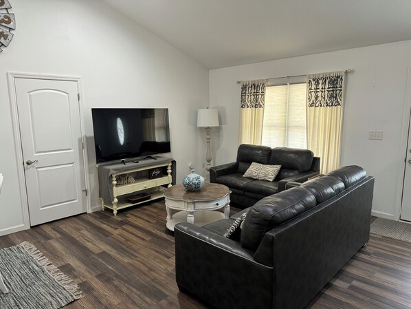 A living room with a sofa, a coffee table, a TV, and a door. - Lake Life Getaway! (Winchester)