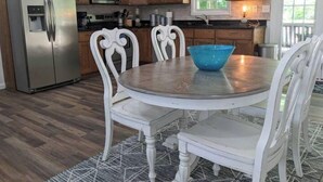 A kitchen with wooden cabinets, a stainless steel refrigerator, a microwave, and a dining table with white chairs. - Lake Life Getaway! (Winchester)