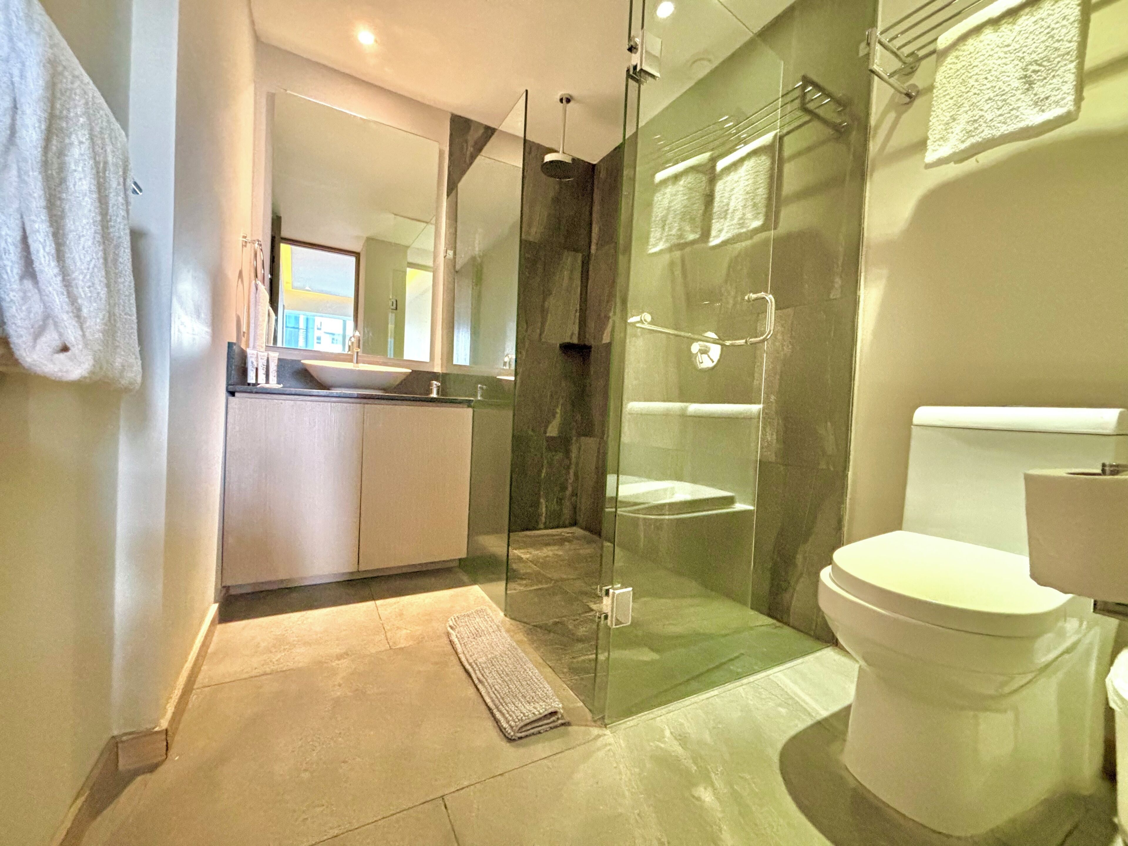 A modern bathroom with a glass-enclosed shower, a white toilet, and a sink with a mirror above it.