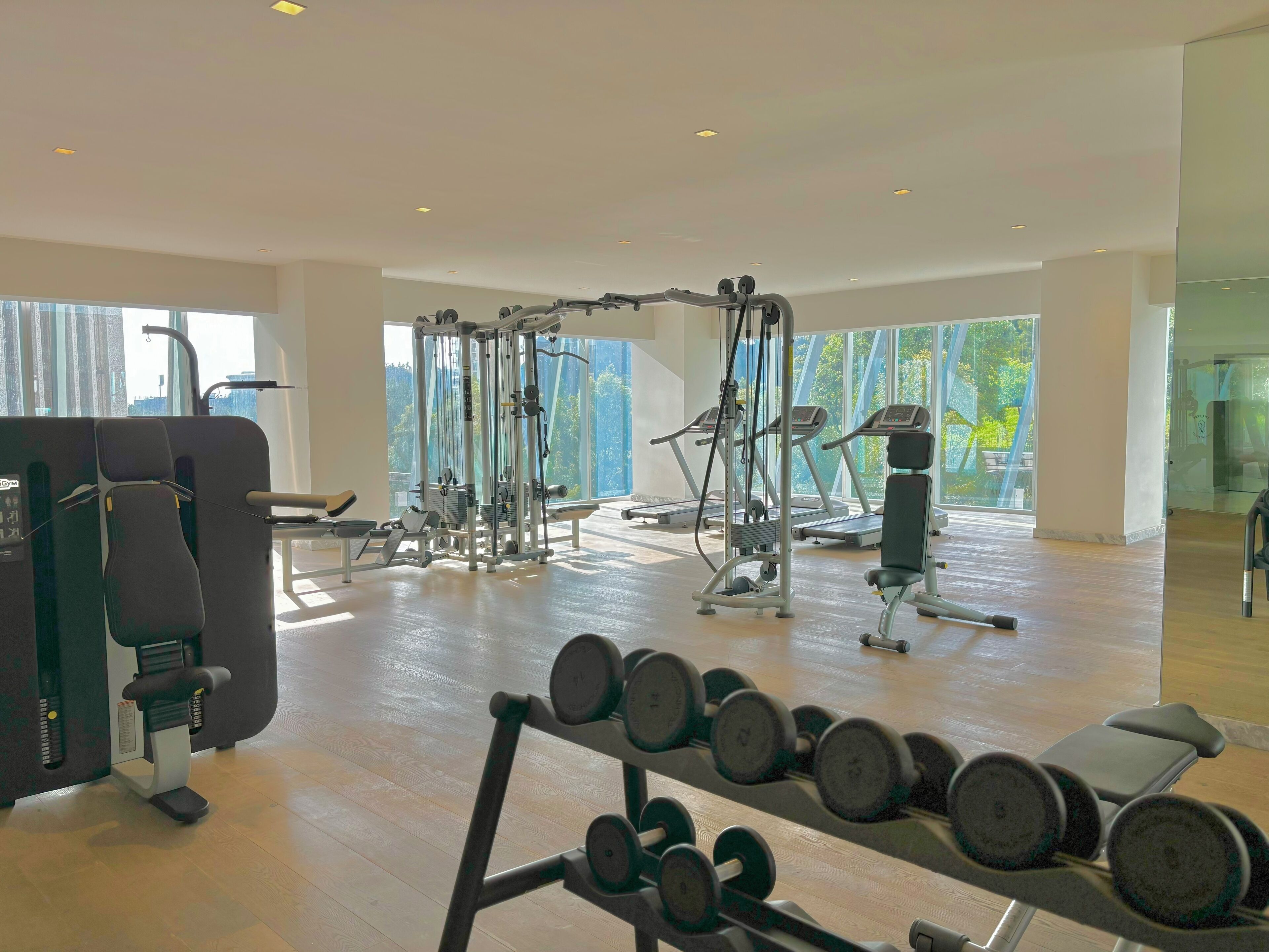 Uma academia espaçosa com diversos equipamentos de exercício, janelas amplas e piso de madeira.