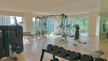 A spacious gym with various exercise equipment, large windows, and a wooden floor.