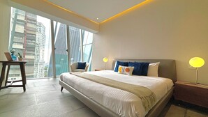 Habitación de hotel moderna con una cama grande, un escritorio con una computadora portátil y vistas a edificios altos por la ventana.