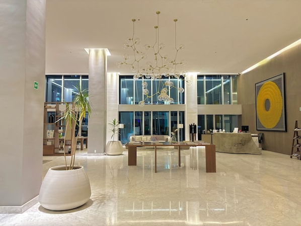 A spacious lobby with a modern chandelier, a reception desk, and a large abstract painting.