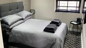 A modern hotel room with a large bed, a wall clock, a window with blinds, and a small table with a kettle. - The Stables at The Black Horse (Crook)