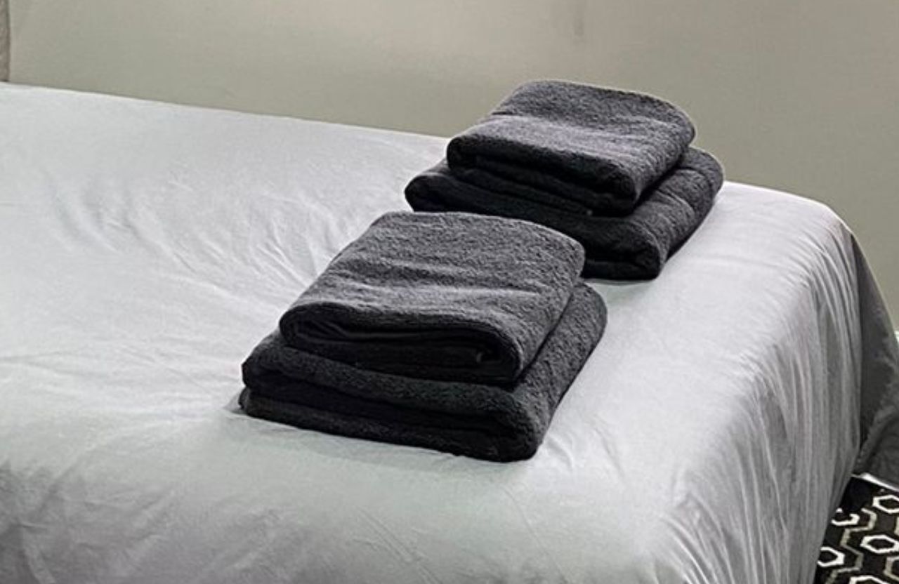 Un lit bien fait, avec des serviettes sombres pliées posées sur la tête de lit.