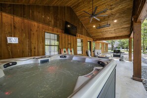 A wooden cabin with a hot tub, a ceiling fan, and a grill area.