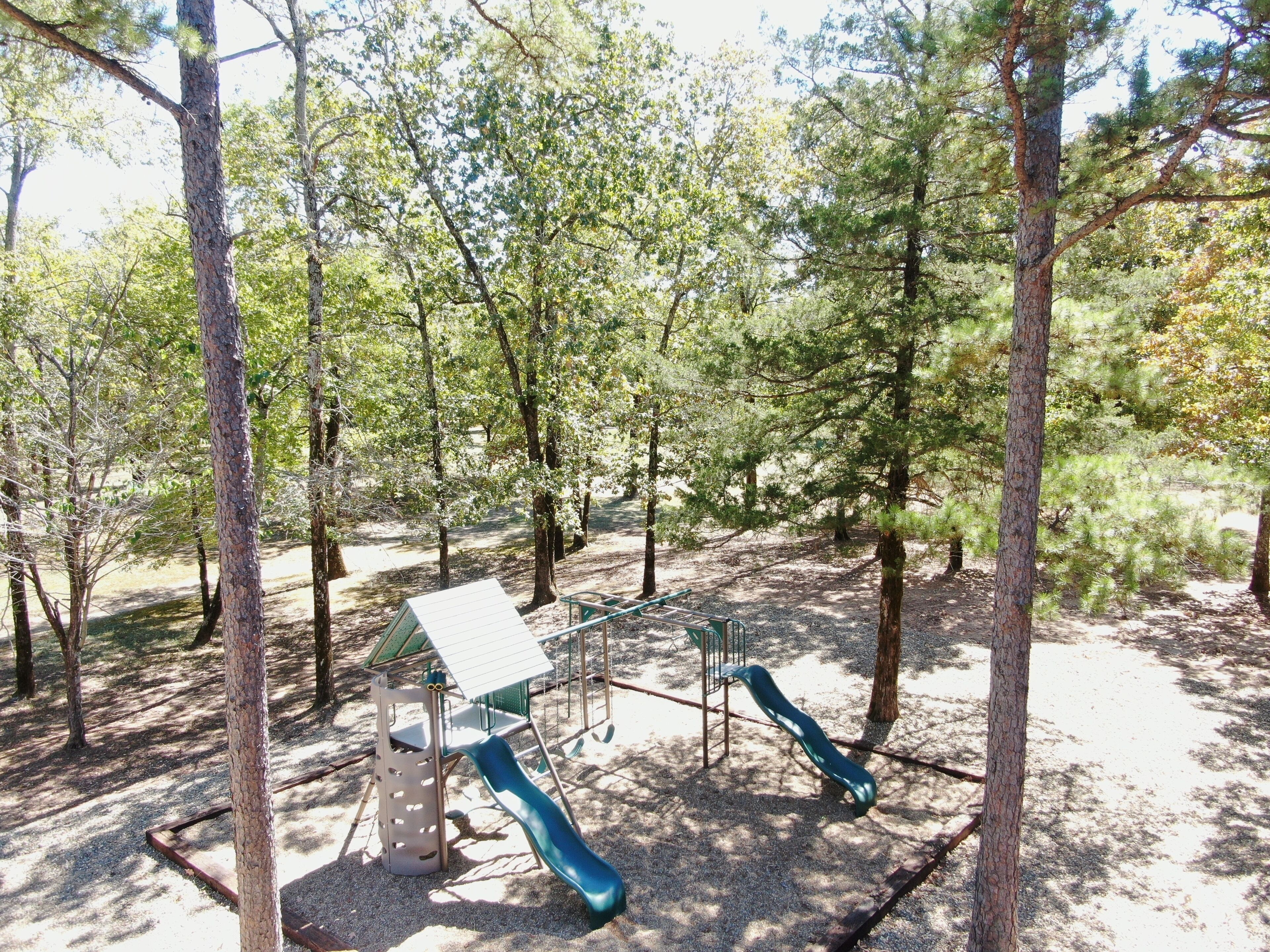 Un parque infantil con tobogán y estructuras para escalar, rodeado de árboles.