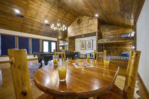 A wooden-floored room with a pool table, a dining table with chairs, and a loft bed.