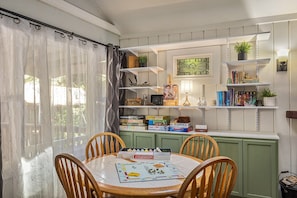 A dining area with a table set for four, surrounded by wooden chairs. There are shelves above the table holding books, decorative items, and a small plant.
