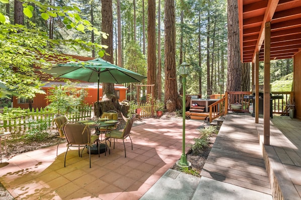 Une terrasse en bois, agrémentée de mobilier d’extérieur, entourée de grands arbres.