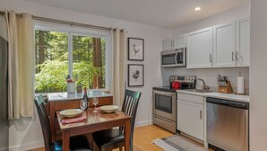 Une cuisine moderne avec des meubles blancs, des appareils en acier inoxydable et un coin repas comprenant une table et des chaises en bois.