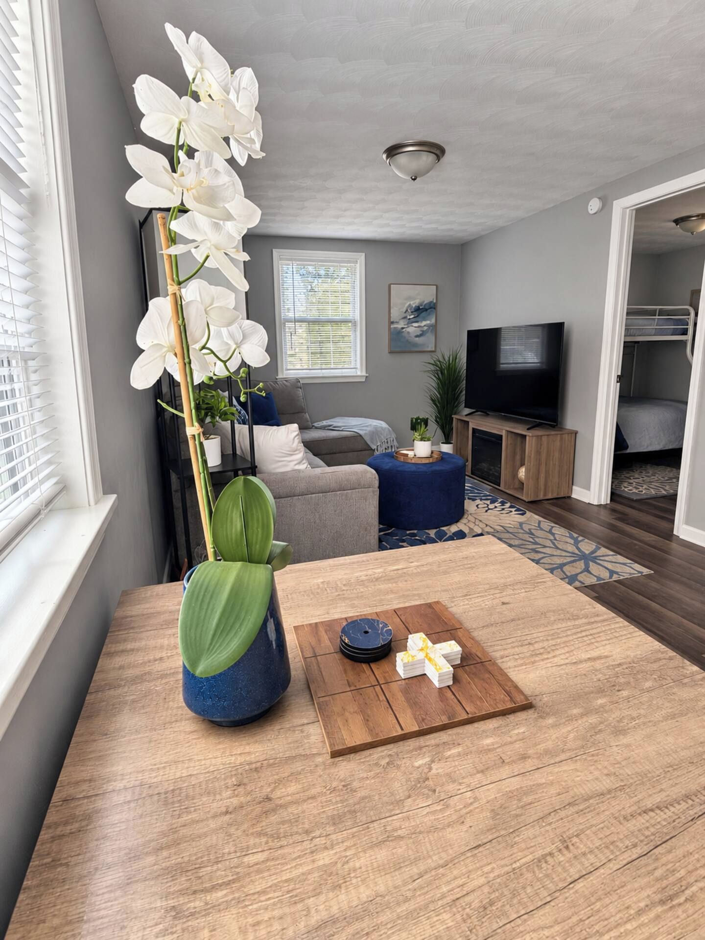 A modern living room with a wooden coffee table, a large white orchid, and a flat-screen TV.