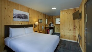 A hotel room with a large bed, wooden walls, a mounted TV, a small kitchenette, and a picture of bison on the wall. - The Cozy Mountain's Edge (Hill City)