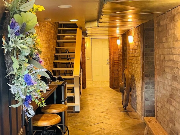Um corredor estreito com escada de madeira, um ventilador e um arranjo floral decorativo.