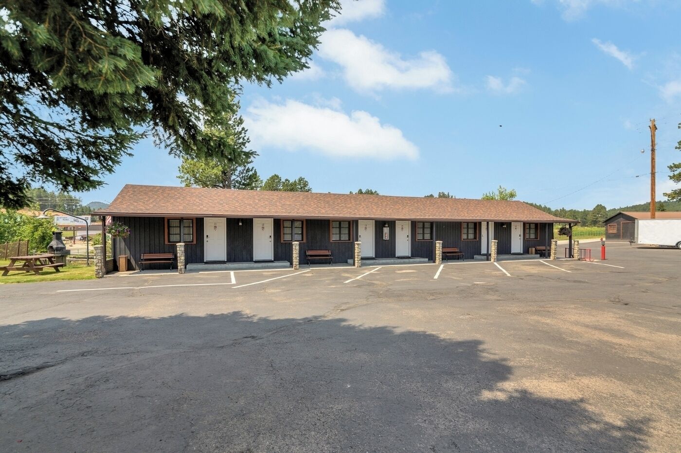 Un motel con una fila de habitaciones, una zona de estacionamiento techada y una mesa de picnic.