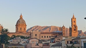 Paesaggio urbano con edifici storici, tra cui una cupola imponente e un campanile, sullo sfondo di montagne.