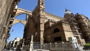 Un arco in pietra storica che conduce a un edificio imponente, con elaborate decorazioni intagliate e un'alta torre.