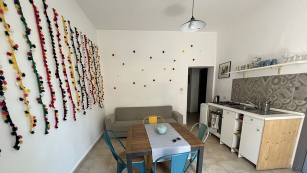 Una cucina compatta con zona pranzo, che include un divano, un tavolo con sedie e una parete con decorazioni colorate.