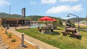 Un área junto a la piscina con mesas de picnic, una parrilla y una zona de estar cubierta.