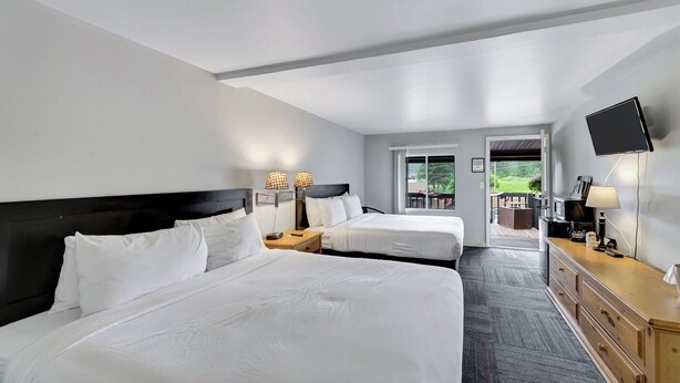 A hotel room with two beds, a flat-screen TV, a wooden dresser, and a balcony with outdoor seating. - Pine Top Balcony View (Hill City)