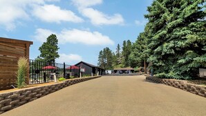 A paved driveway leading to a building with a red roof, surrounded by trees and a wooden fence. - Pine Top Balcony View (Hill City)