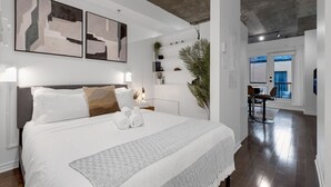 A modern bedroom with a large bed, abstract wall art, a plant, and a view of the living area. - Suite 407 Downtown Montreal | W/ Balcony, Queen Bed, Sofa Bed, Parking & 55` TV (Montréal)
