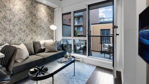 A modern living room with a grey sofa, a coffee table, and a large window with a view of a building and a balcony. - Suite 407 Downtown Montreal | W/ Balcony, Queen Bed, Sofa Bed, Parking & 55` TV (Montréal)