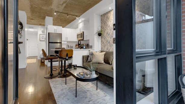 A modern kitchen with white cabinets, a microwave, and a coffee machine. There is a dining area with a table and chairs, and a sofa in the living room. - Suite 407 Downtown Montreal | W/ Balcony, Queen Bed, Sofa Bed, Parking & 55` TV (Montréal)