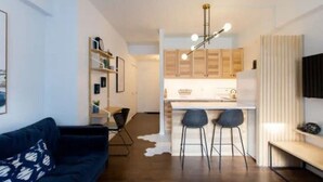 Una sala de estar moderna con un sofá azul oscuro, una mesa de centro y una cocina con armarios de madera y un taburete de bar.