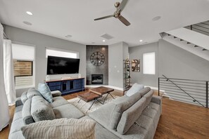 A modern living room with a flat-screen TV, a fireplace, and a staircase.