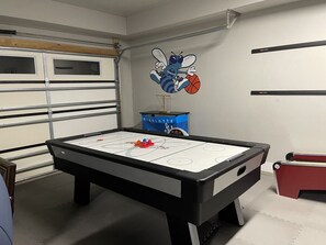 A pool table with a blue and red puck in the center, a Charlotte Hornets logo on the wall, and a red storage box to the right.