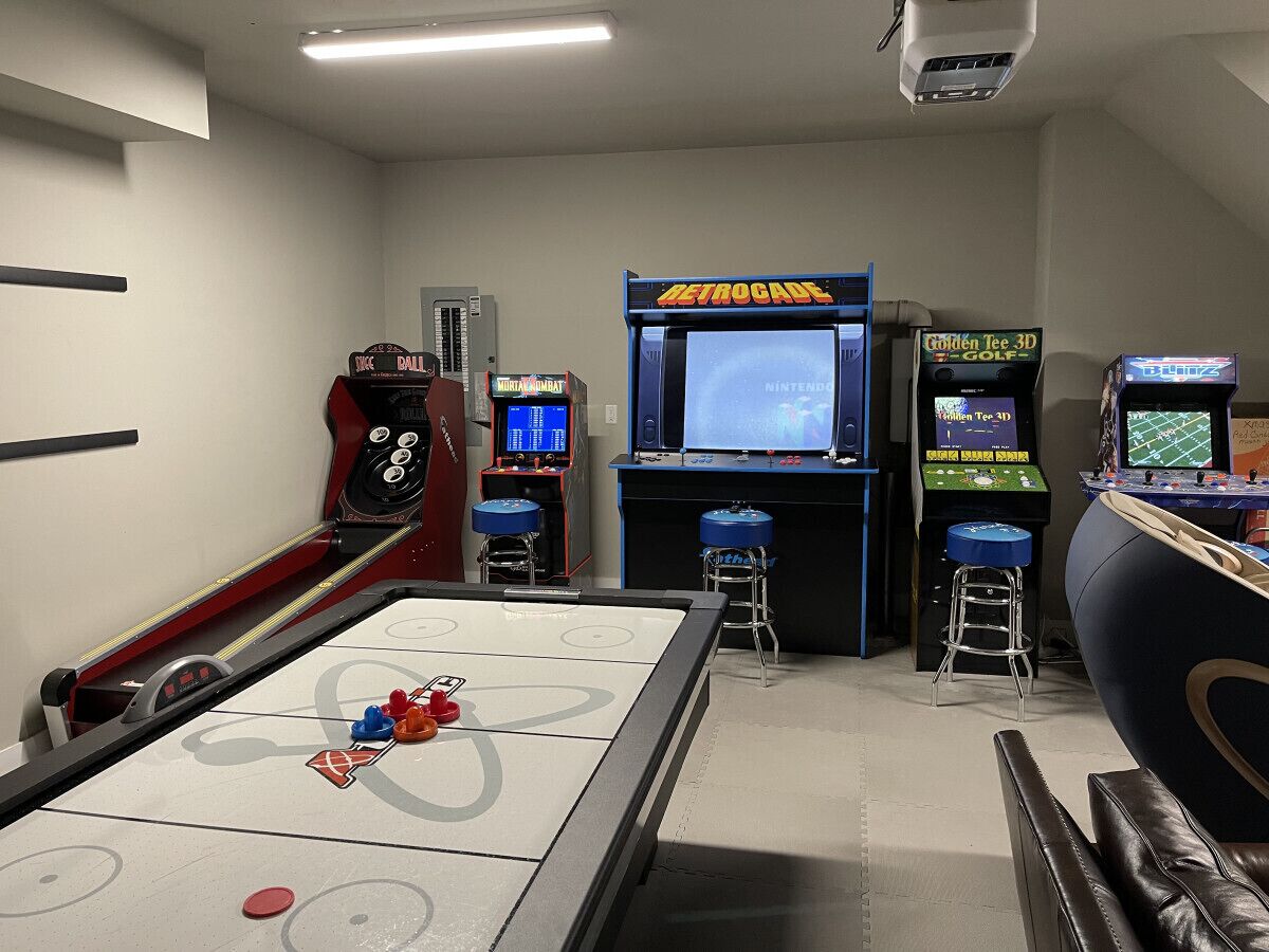 A room with a shuffleboard table, a Nintendo 64 console, and a Golden Tee 3D Golf arcade machine.