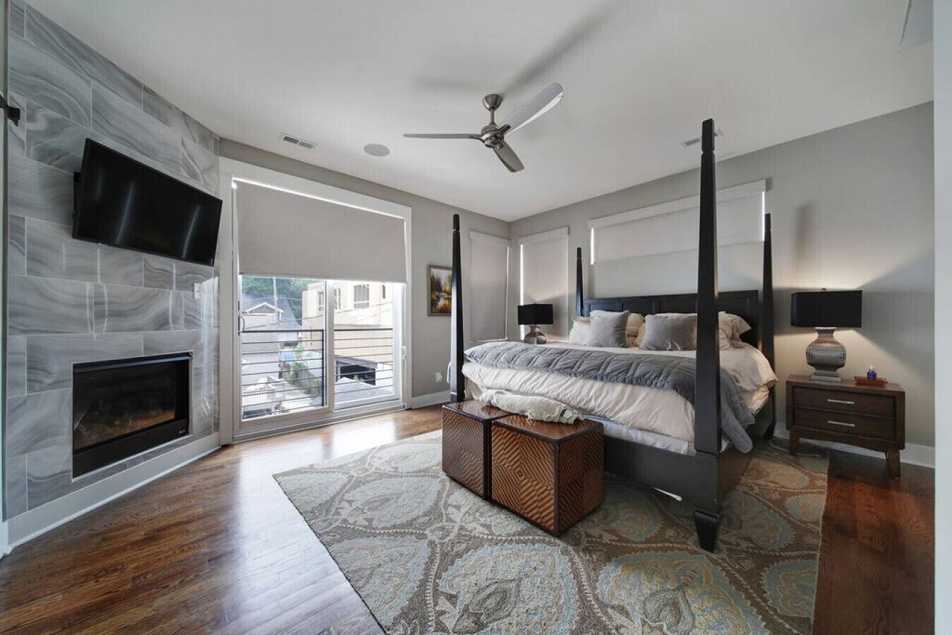 Une chambre à coucher avec une cheminée, un lit, une table de chevet, un ventilateur de plafond et une grande fenêtre.