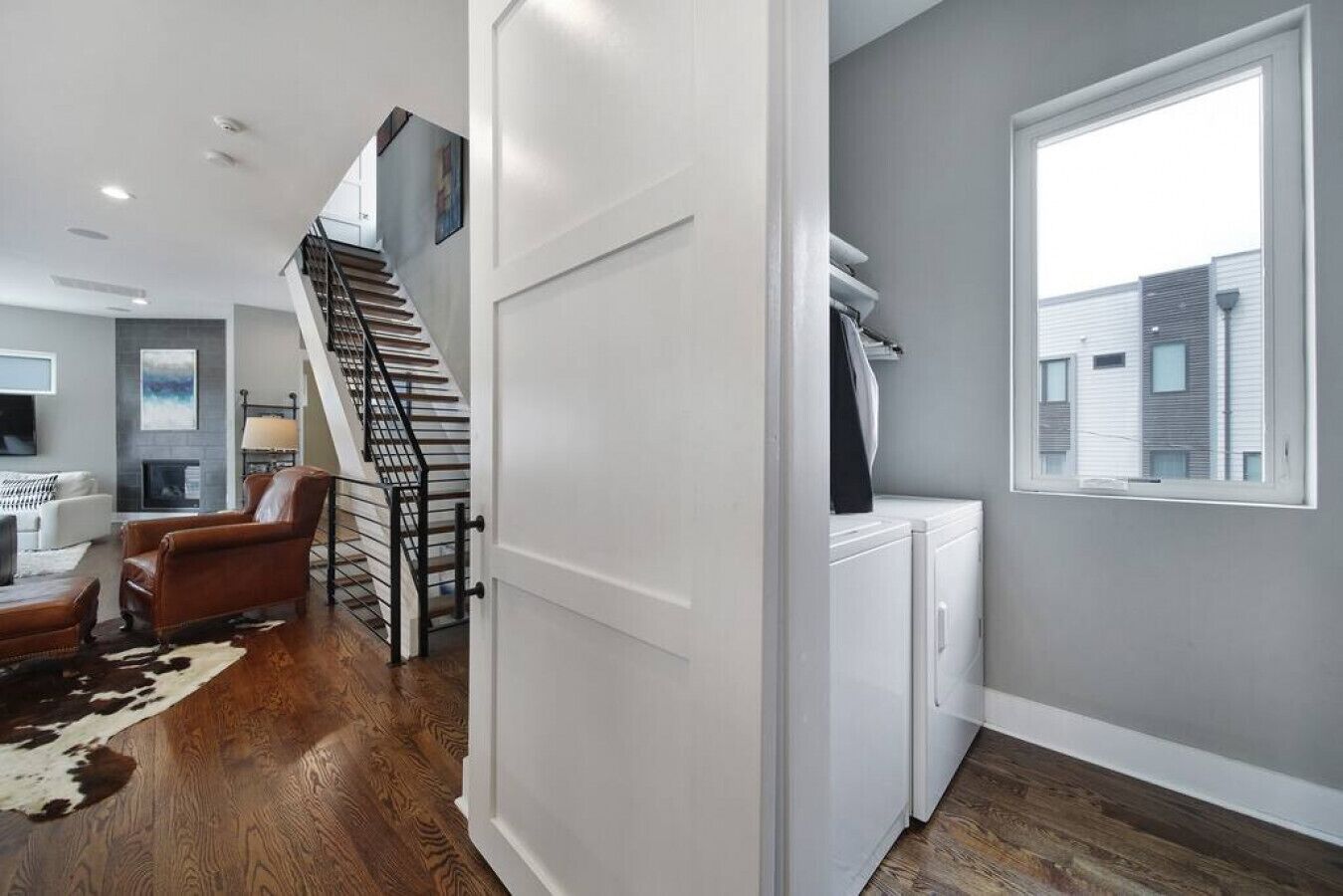 Un intérieur moderne comprenant un escalier, un espace de vie avec un canapé et un tapis, ainsi qu’un coin buanderie avec un lave-linge.