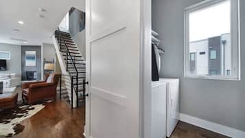 Un intérieur moderne comprenant un escalier, un espace de vie avec un canapé et un tapis, ainsi qu’un coin buanderie avec un lave-linge.