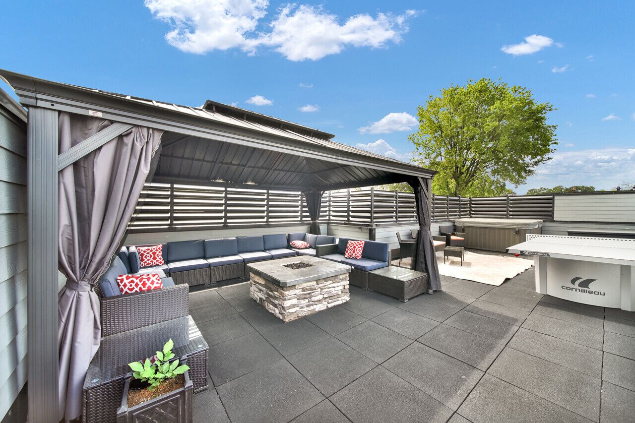 An outdoor patio with a covered seating area, a stone fire pit, and a grill station.