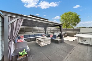 An outdoor patio with a covered seating area, a stone fire pit, and a grill station.