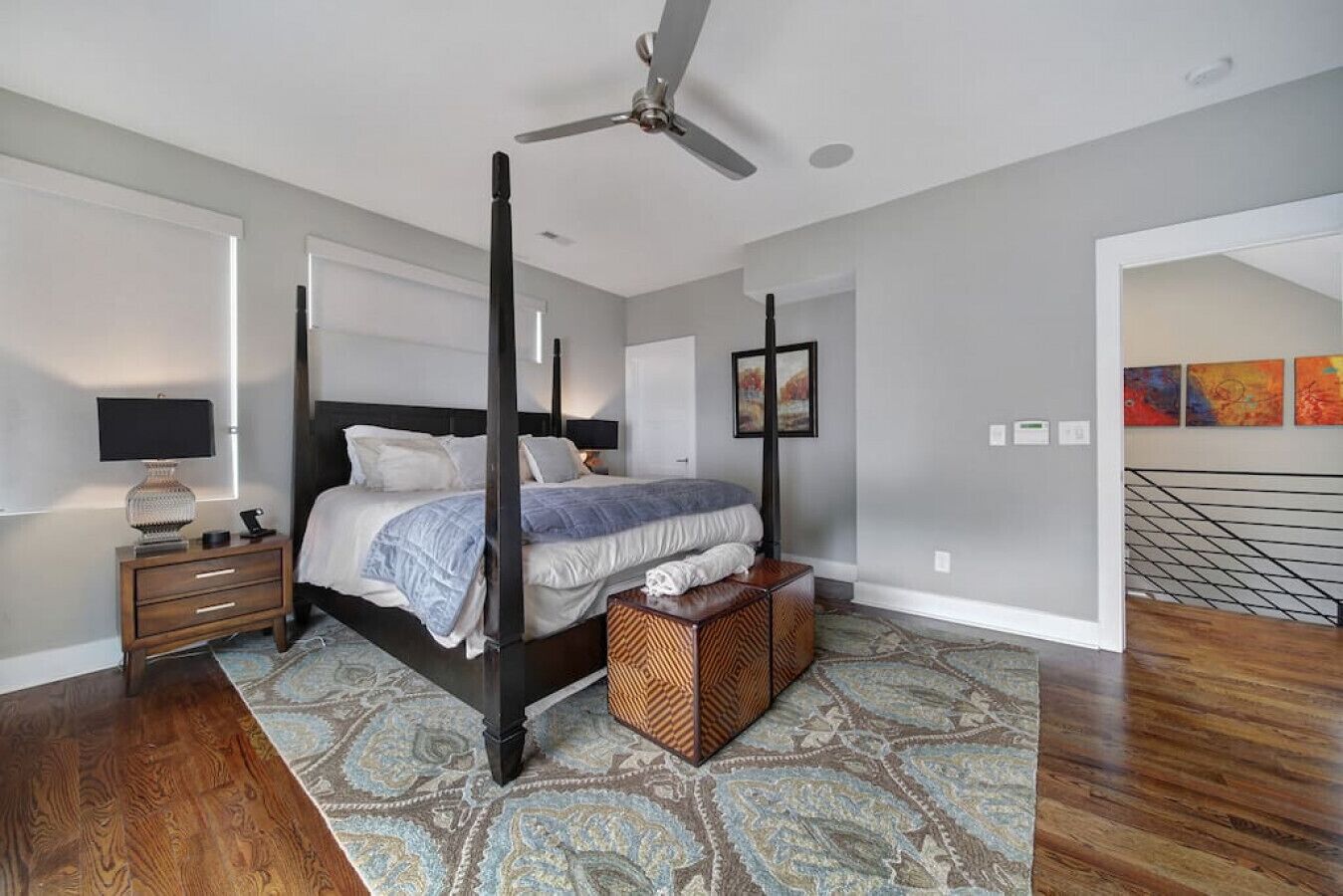 A four-poster bed with a dark finish, a standing lamp, and a patterned rug on a wooden floor.
