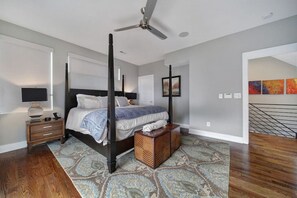 A four-poster bed with a dark finish, a standing lamp, and a patterned rug on a wooden floor.