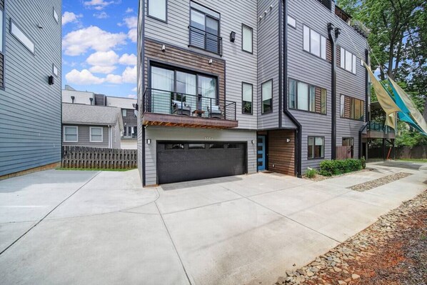 A modern multi-story residential building with a garage, large windows, and a covered entryway.