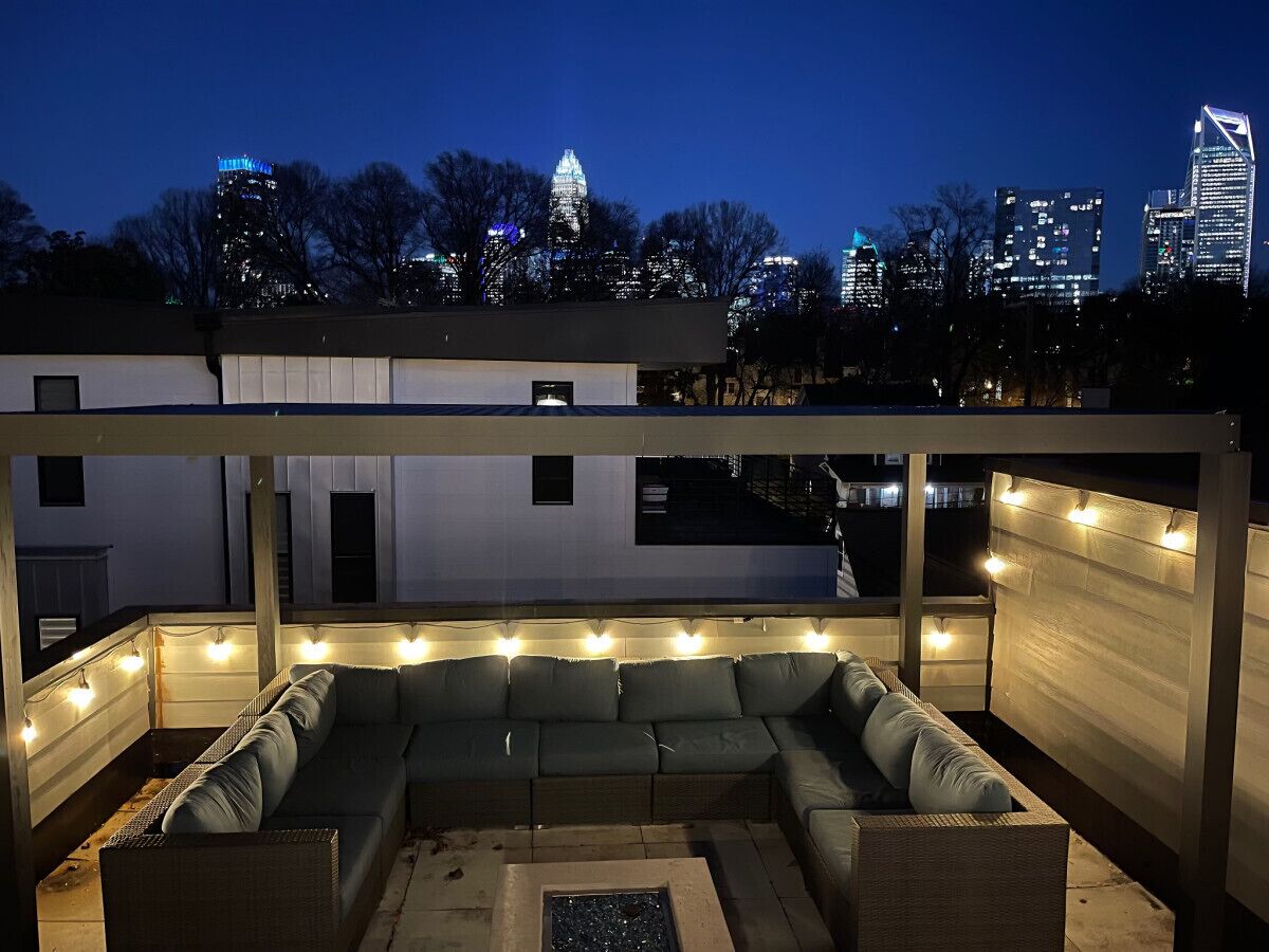An outdoor seating area with a sofa and lights, overlooking a cityscape at night.