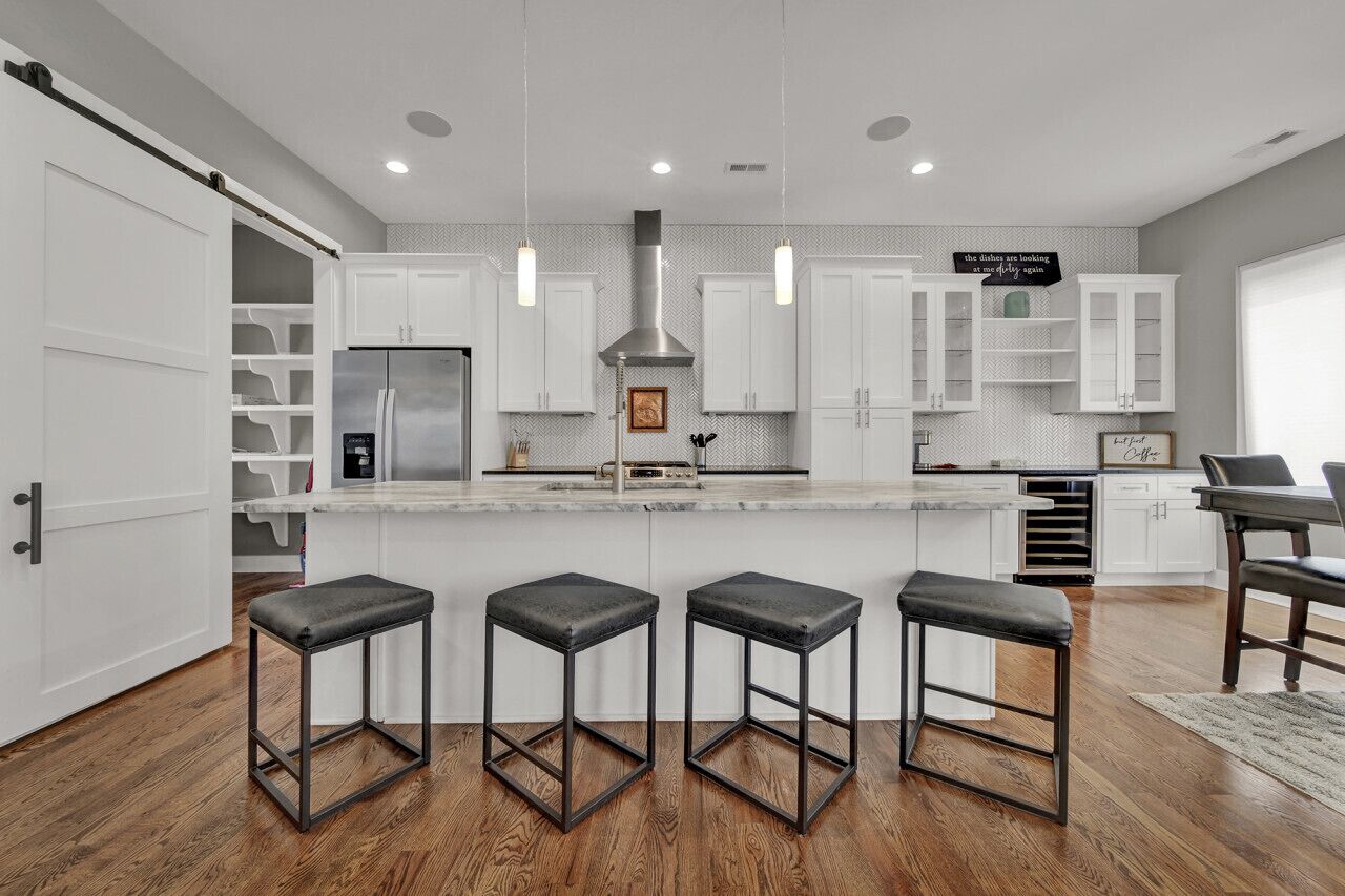 A modern kitchen with white cabinets, a central island with stools, and pendant lighting.