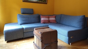 Uma sala de estar com um sofá azul, um baú de madeira e um quadro na parede.