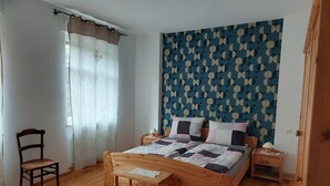 Quarto com cama de madeira, uma cadeira, mesa de cabeceira e parede com padrão geométrico.