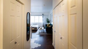 A hallway leading to a bedroom with a bed, a dresser, and a nightstand. There is a mirror on the wall and a plant in the corner.