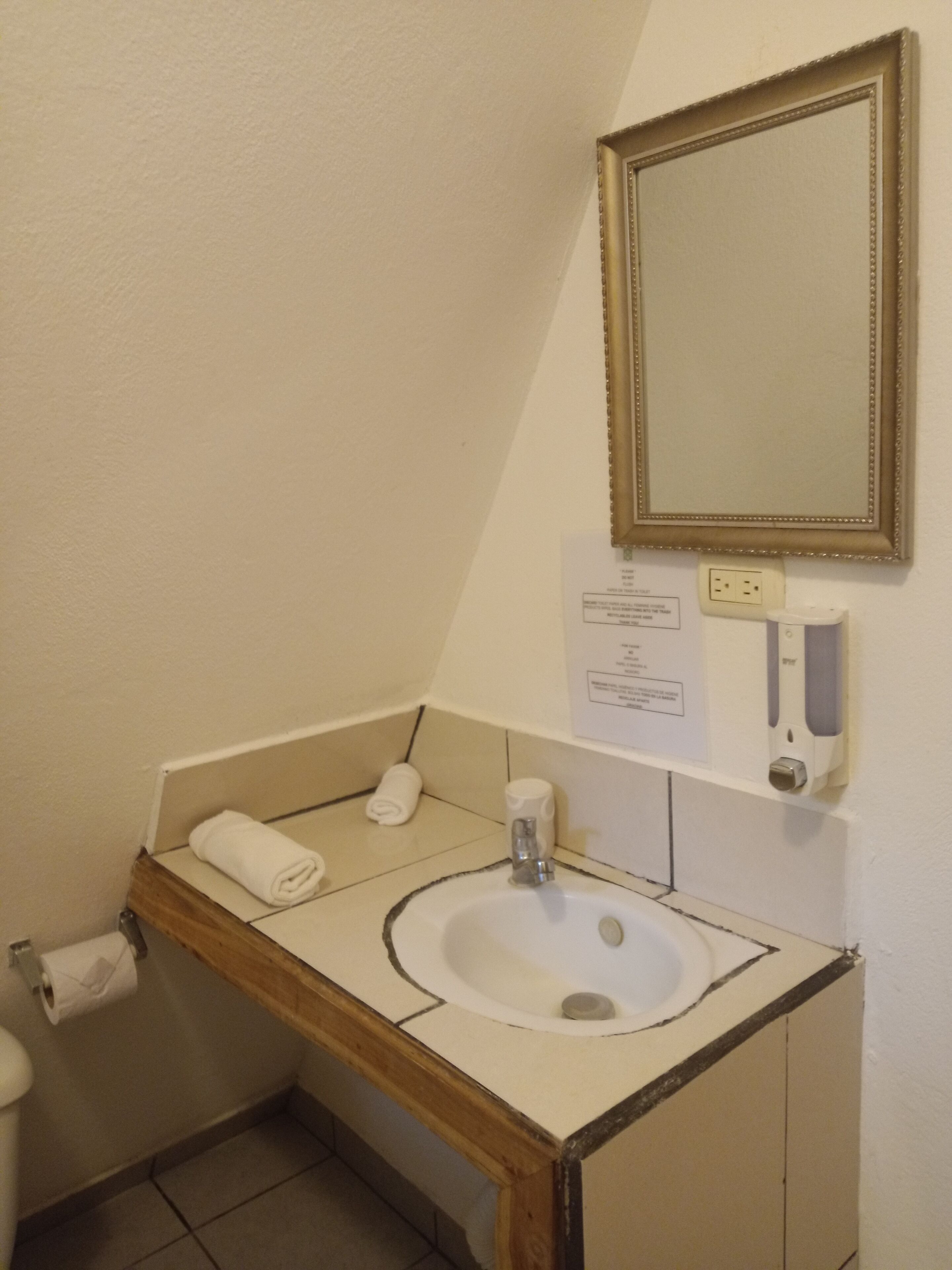 A bathroom with a sink, mirror, towel, and soap dispenser.