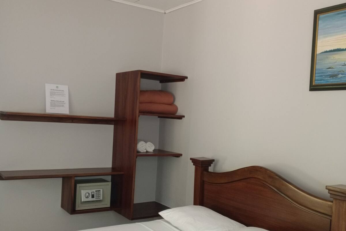 A neatly made bed with a wooden headboard, a small bedside table, and a wall-mounted shelf with folded towels.